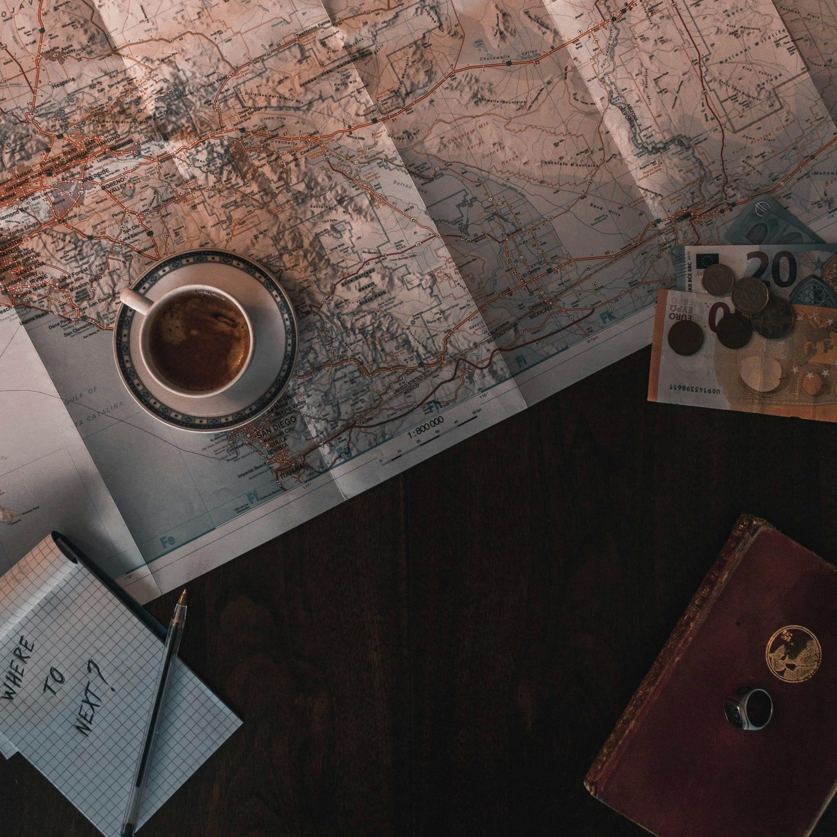 Flat lay of map, coffee, coins, and notebook for travel planning.